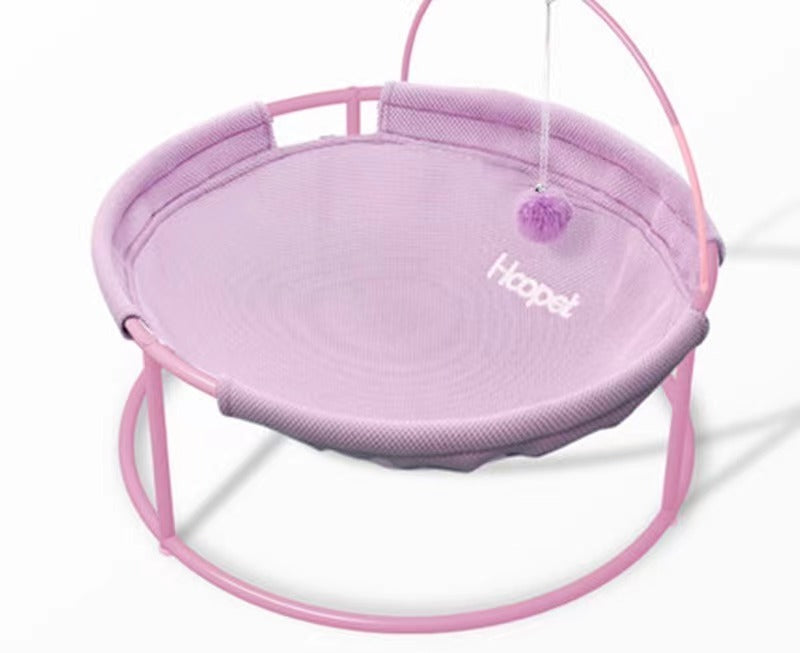 Round hanging pet bed with purple fabric top, pink frame, and hanging pom accessory