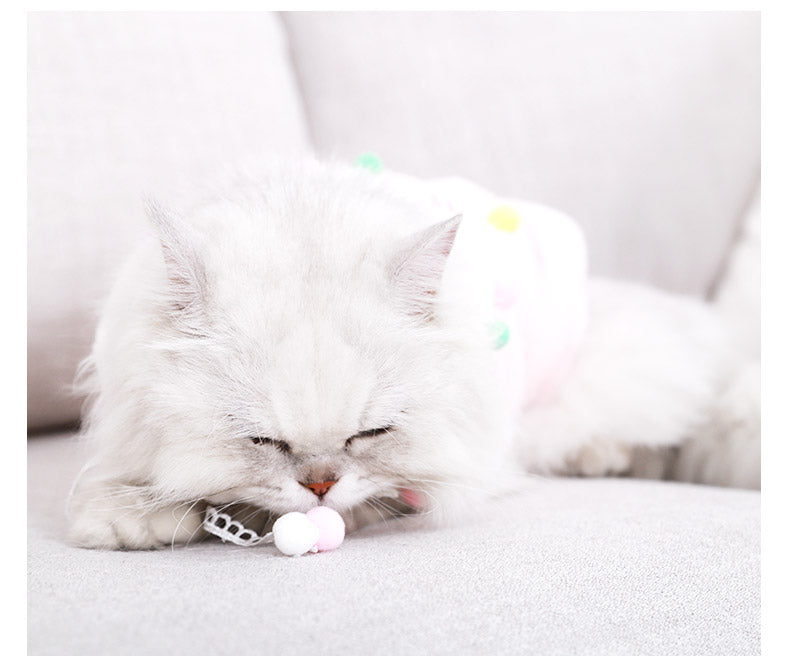 Lightweight pink pet hoodie with lace collar and pom-pom accents on a reclining cat