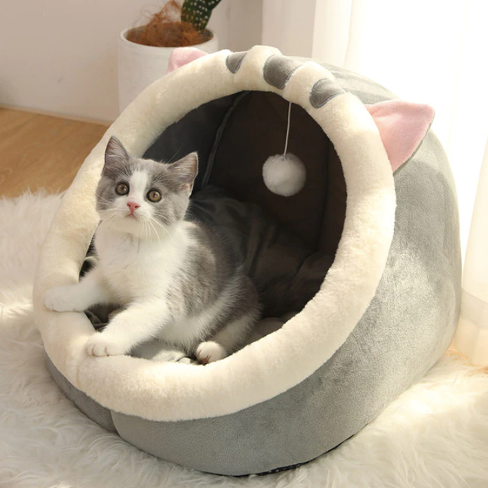 Grey cat bed with cream rim and dangling pom-pom toy; cozy enclosed cave for cats