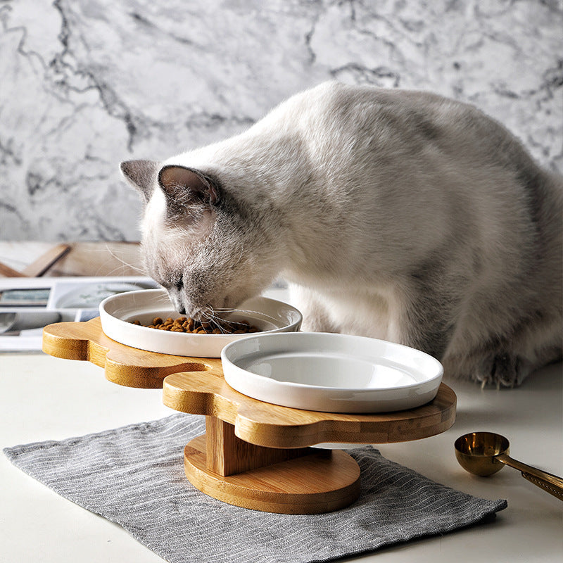 Ceramic cat bowl set with two white bowls on a wooden stand, one being eaten from.