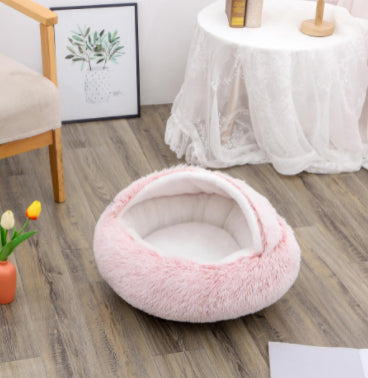 Round plush pet bed in light pink with soft cushioned sides and oval cave opening