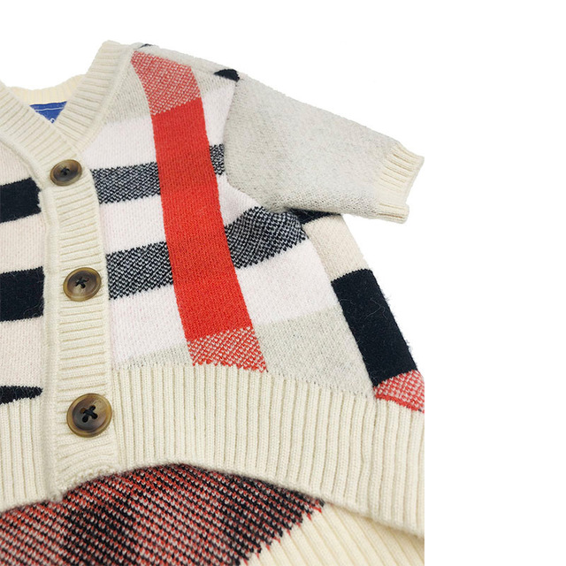 Close-up of cream plaid dog sweater: ribbed sleeves, button placket, black checks and red stripe