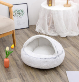 Round plush pet bed in white with padded sides and open oval sleeping cave