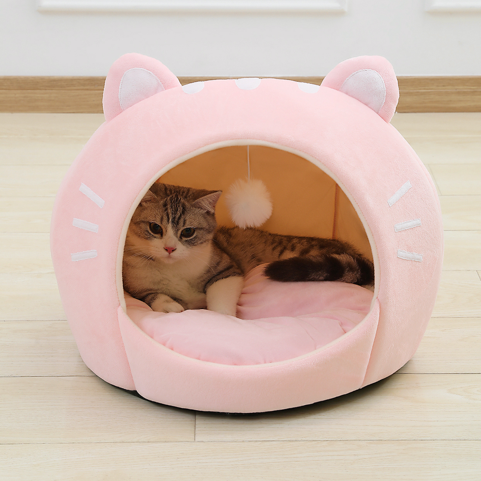 Pink cat-shaped plush pet bed with open entrance and ear hood, tabby cat inside