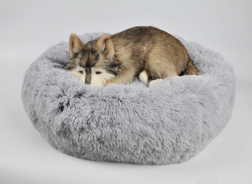 Light gray round plush pet bed with cushioned bolster; dog curled up