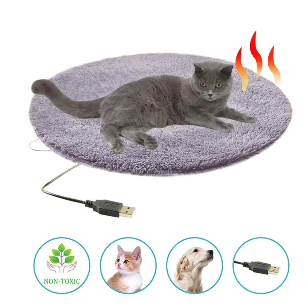 Gray oval heated pet bed mat with resting cat; USB cable shown