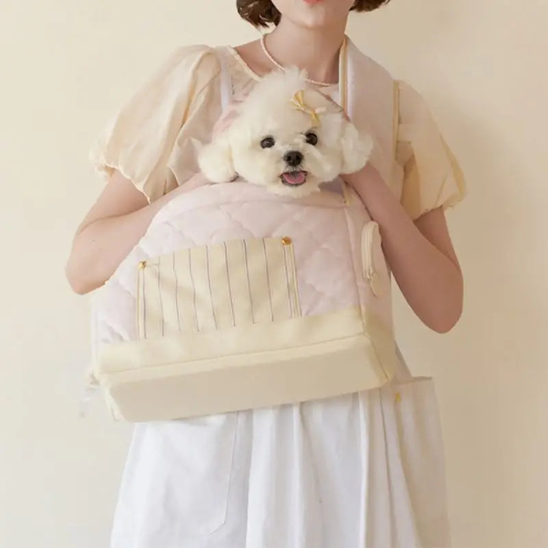 Soft cream pet carrier sling bag with front zipper panel, carrying a small dog on chest
