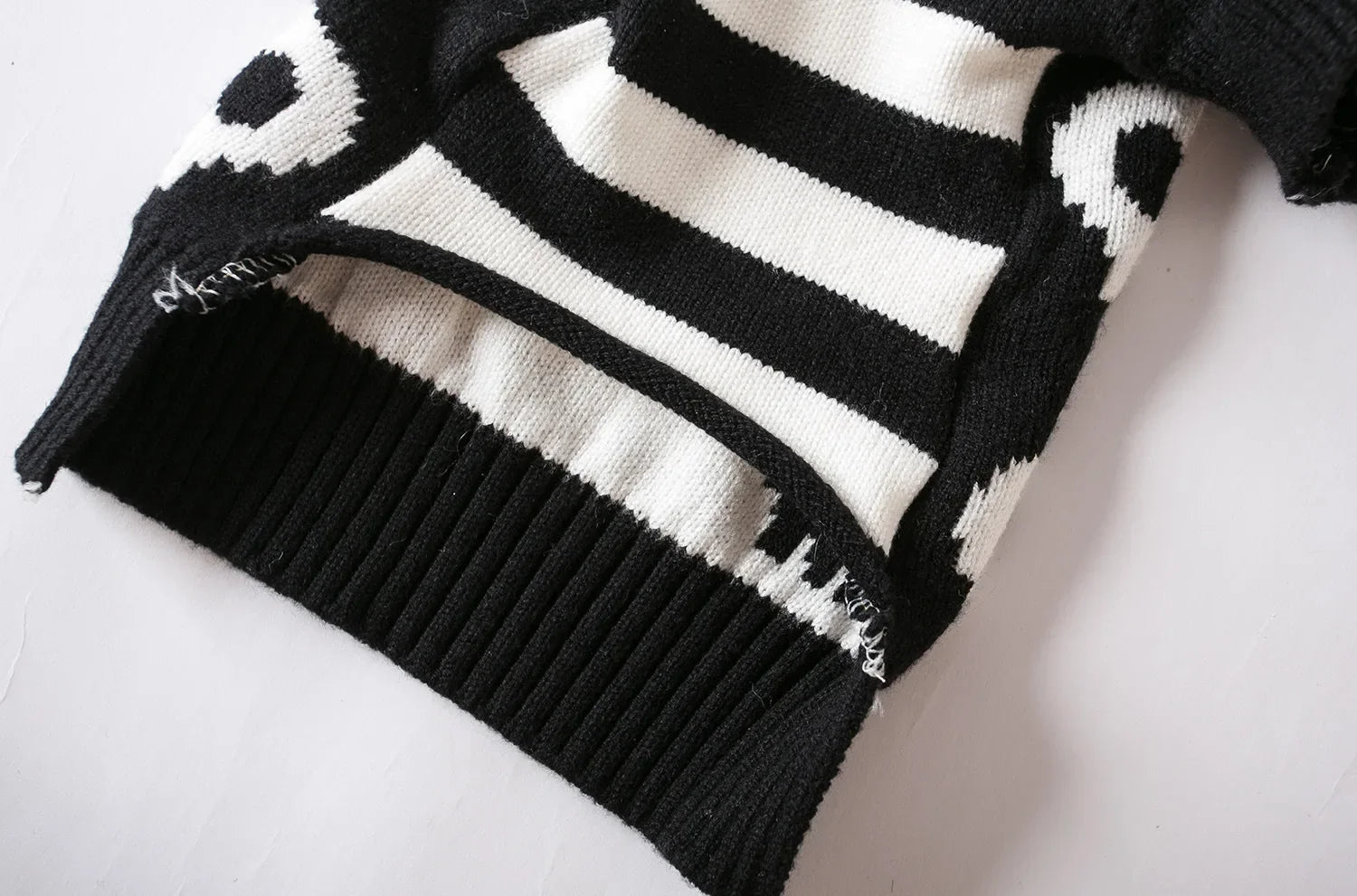Knitted pet sweater hem view, black base with white stripes and partial skulls