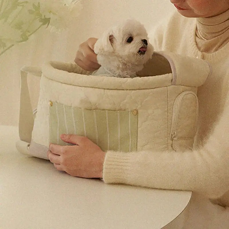 Soft cream cat sling carrier bag with zipper pocket and padded hood, holding a small dog