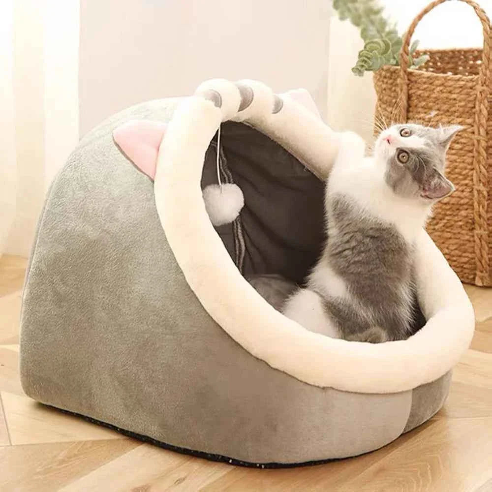 Grey semi-enclosed pet bed with cream opening and hanging pom; British Shorthair inside