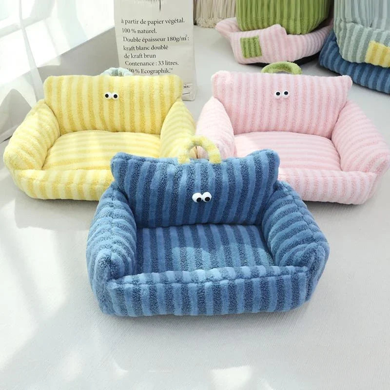 Plush pet sofa bed in blue corduroy with cartoon face, with yellow and pink beds behind