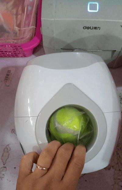 Automatic pet feeder with green tennis ball in the round opening on a white device