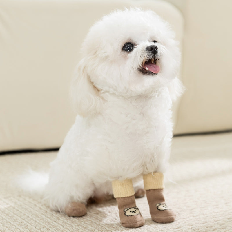 Dog wearing tan long knit socks with cartoon animal face patches at the paws