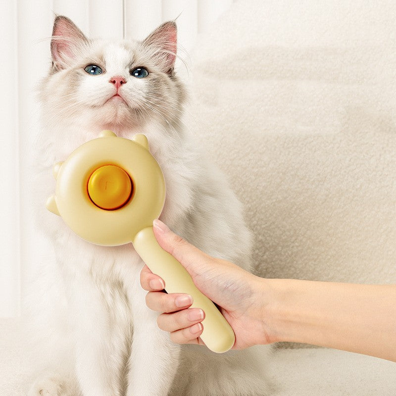 Cat grooming brush with pale yellow rounded massage pad and handle, held near fur