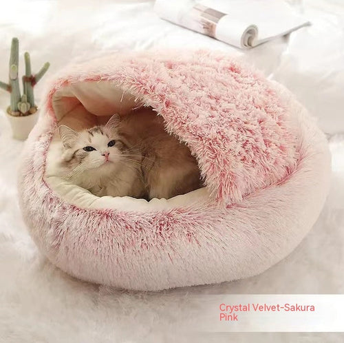 Round plush pet bed in pink, with shaggy exterior and open front cave for pets to rest