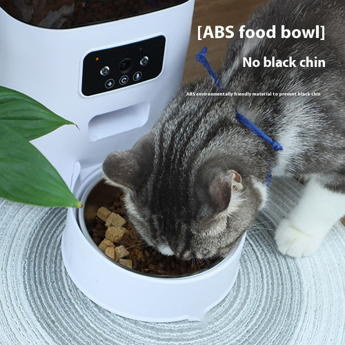 Automatic pet feeder, white base with black top, cat eating from stainless bowl.