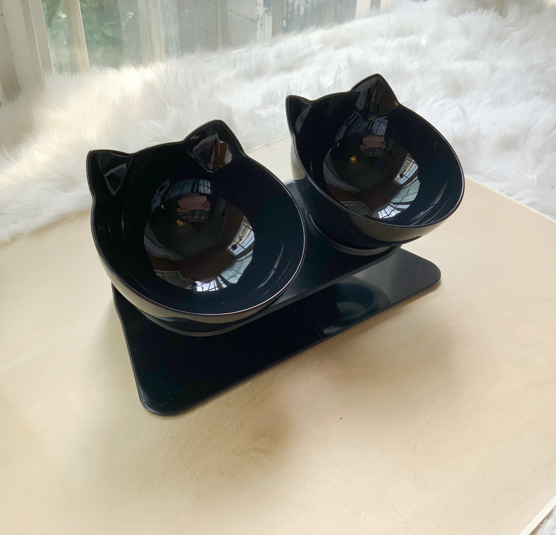 Double black cat-shaped pet food bowls on glossy black raised stand