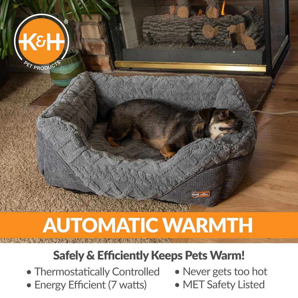 Grey plush heated pet bed with raised bolsters; small dog resting inside