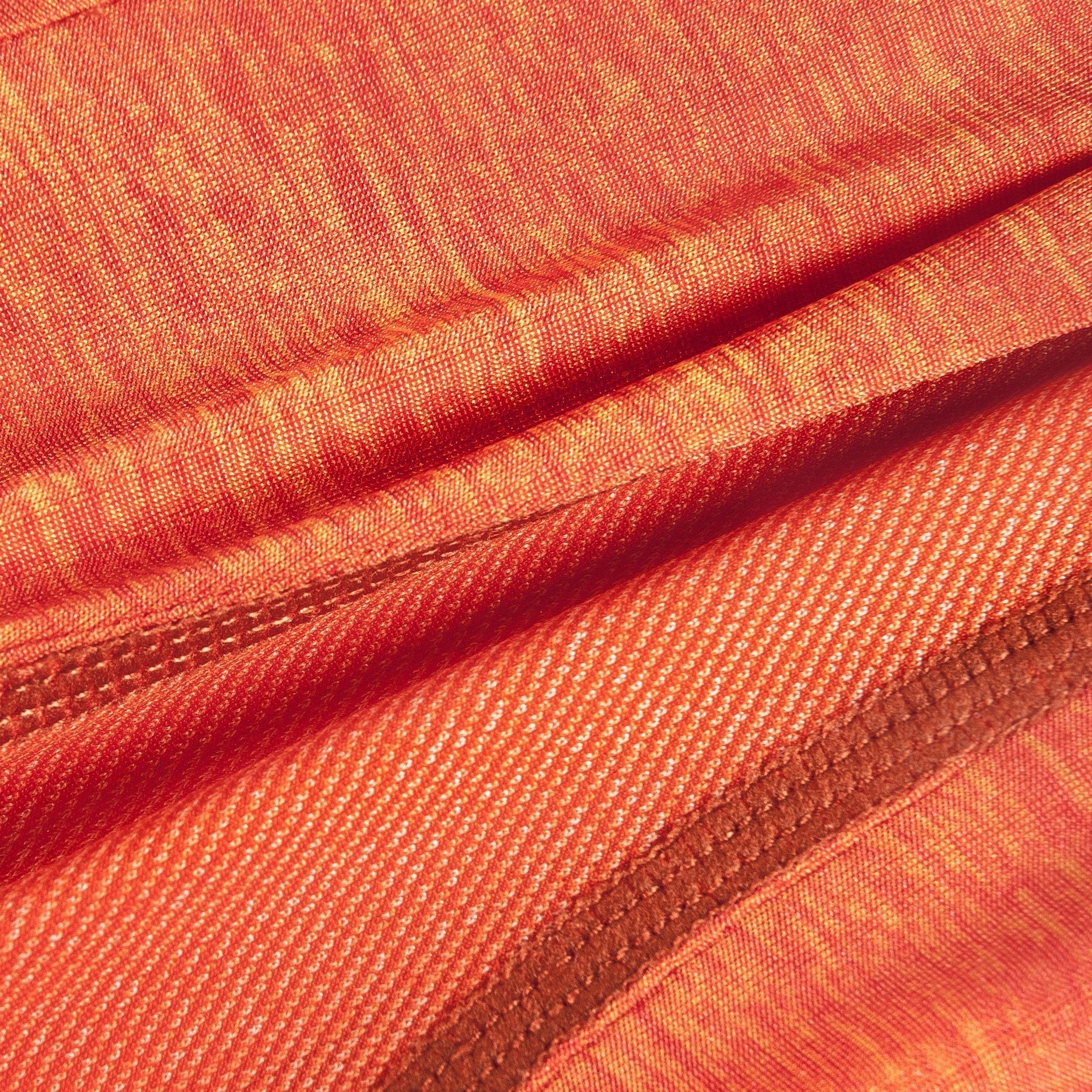 Orange woven fabric close-up with stitched seam along the edge