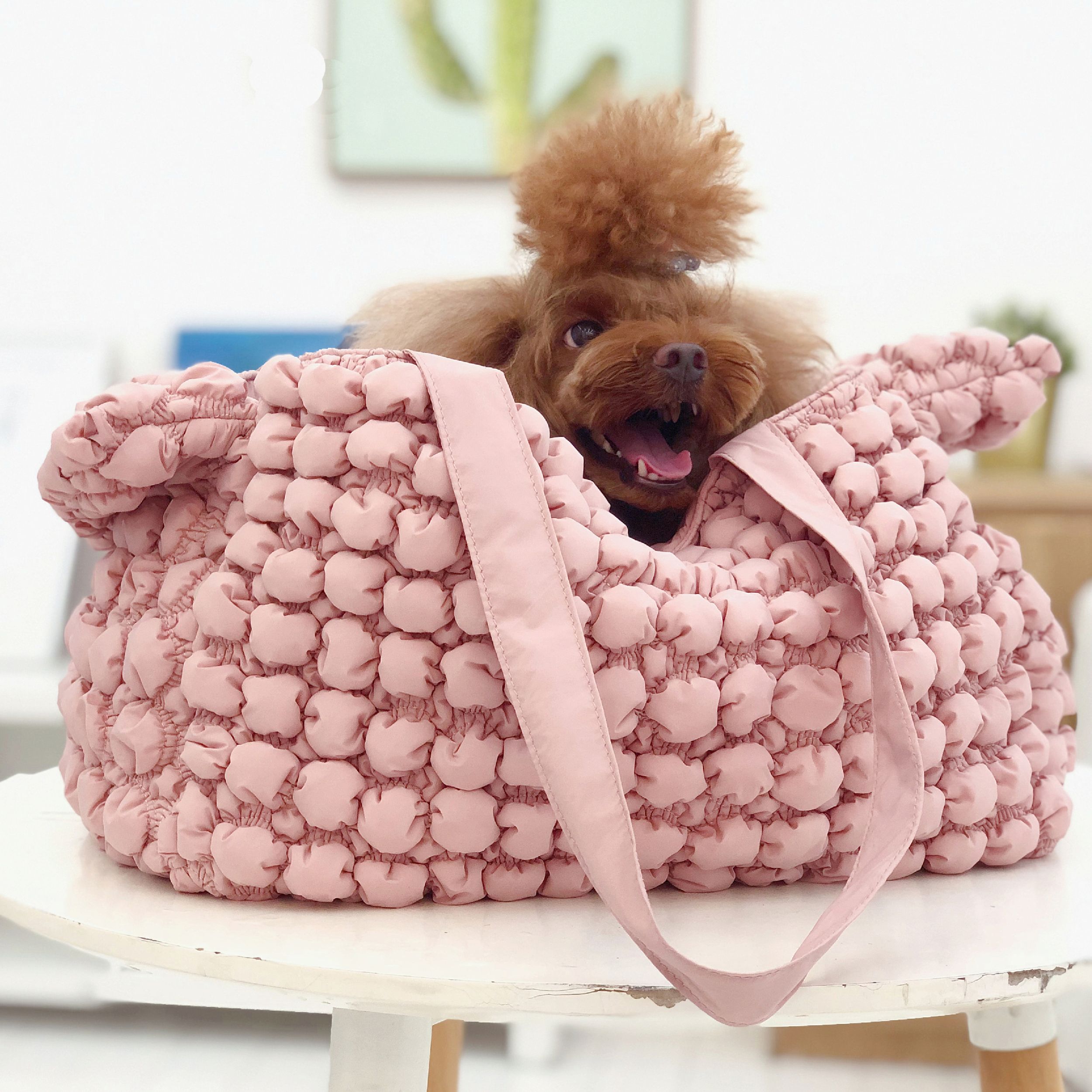 Pink bubble plush pet carrier on stand, with dog peeking out; front handles visible.