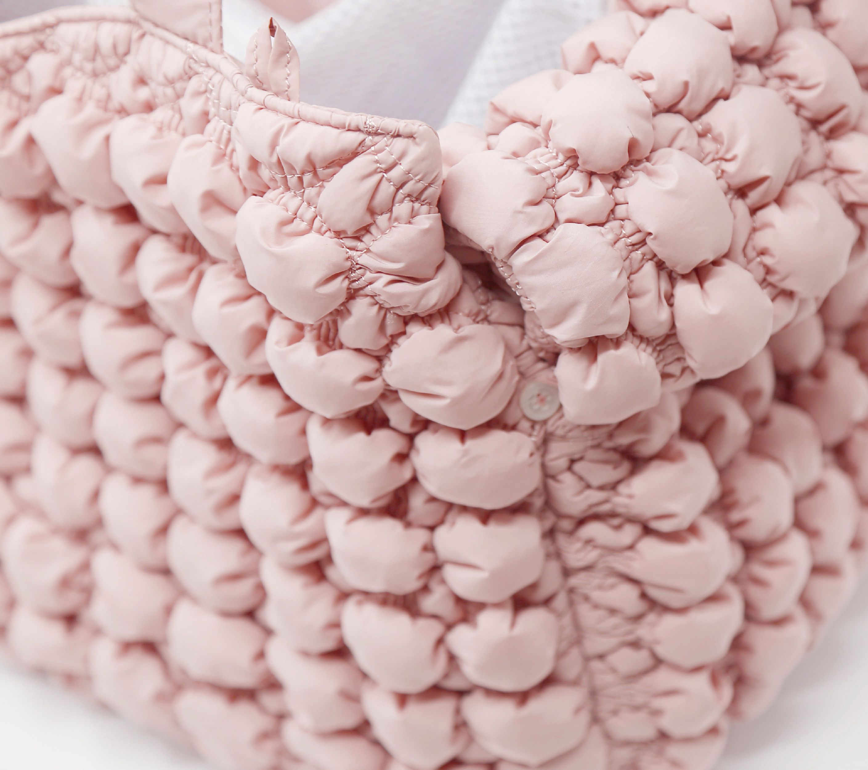 Pink bubble-knit plush pet carrier texture close-up with fabric handles.