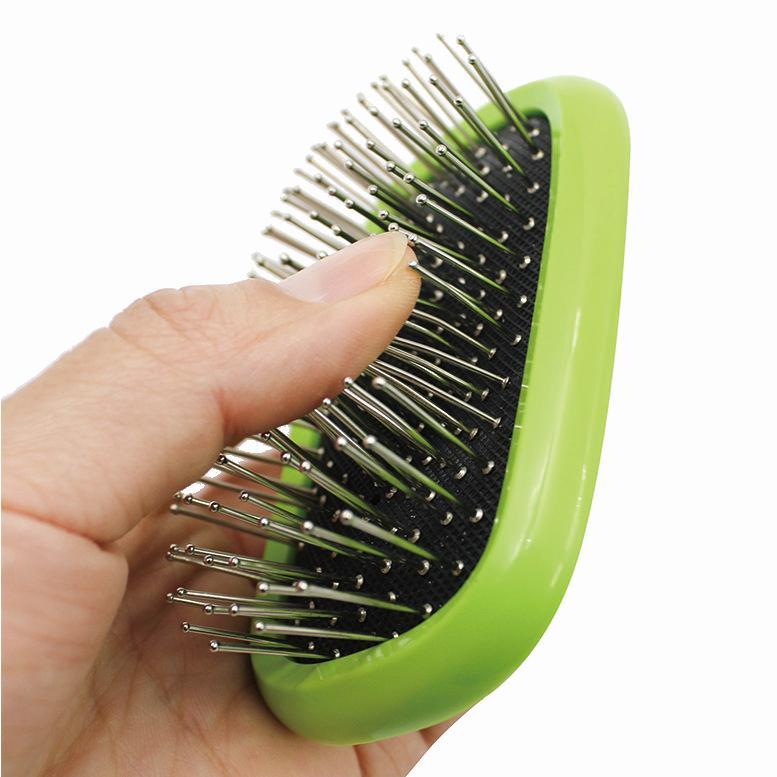 Hand holding green grooming brush head with metal pins on black pad