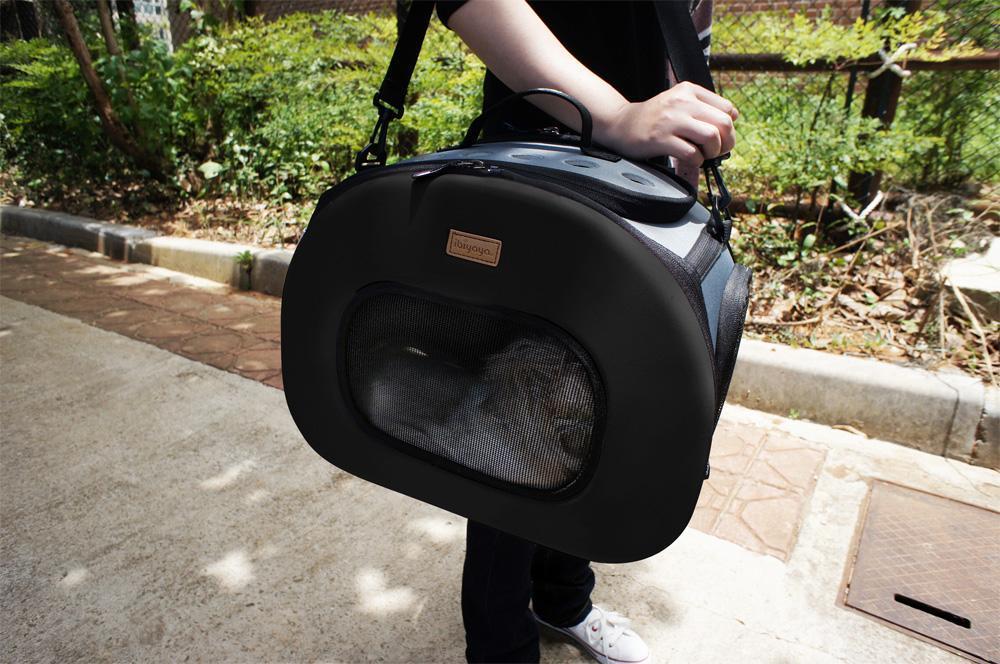 Black tough-shell wheeled pet carrier crate held by the top handle