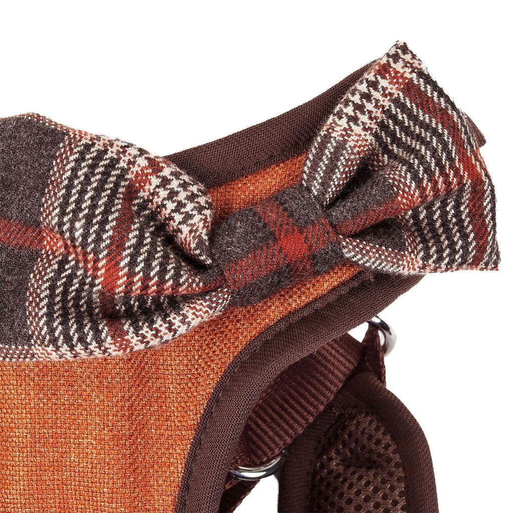 Dog harness close-up: plaid bow detail on orange-brown fabric with brown mesh backing.