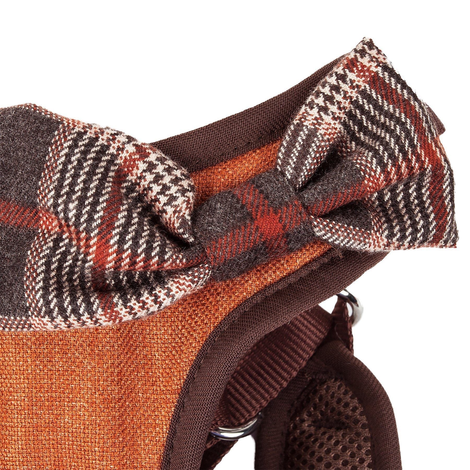 Dog harness close-up: plaid bow detail on orange-brown fabric with brown mesh backing.