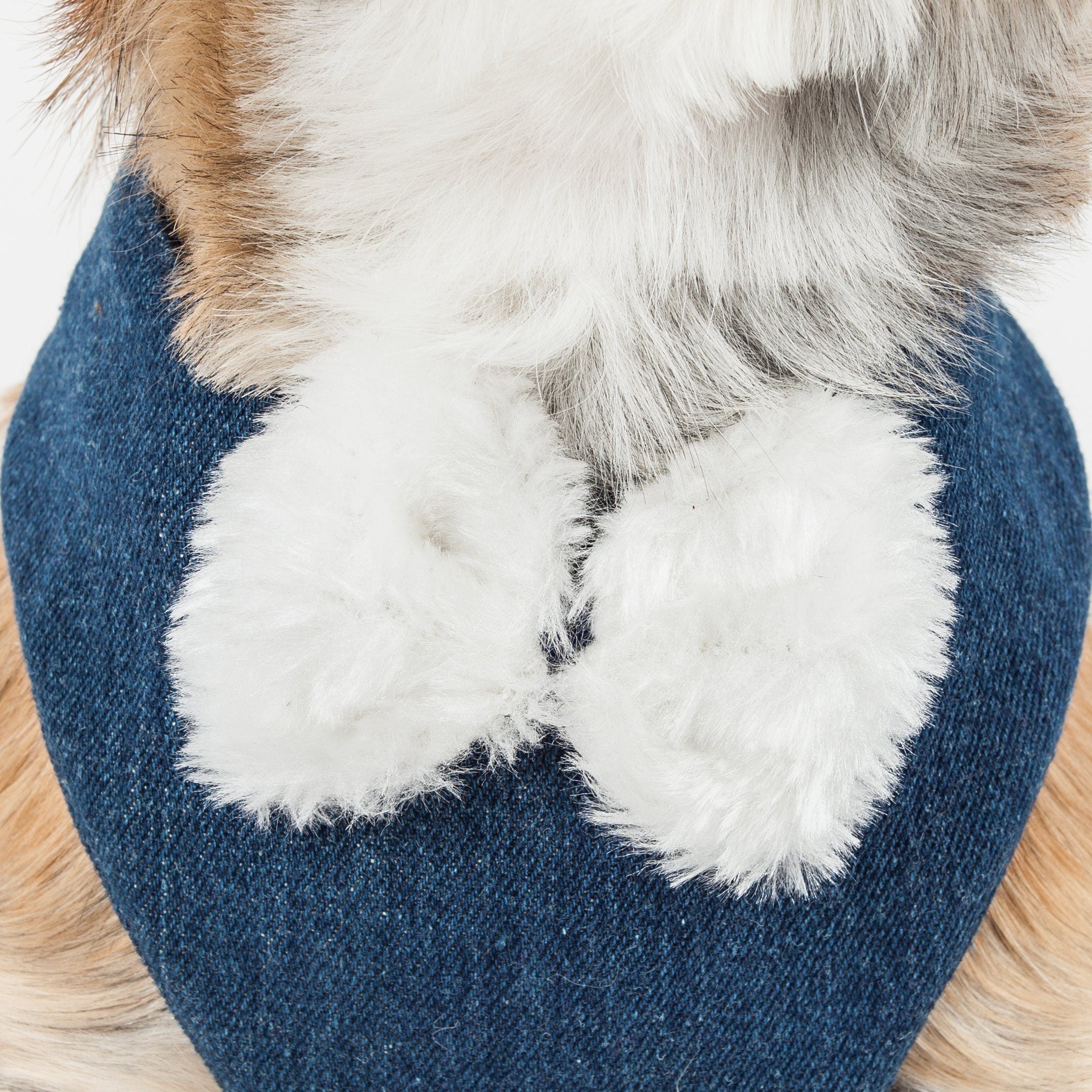 Close-up of white faux-fur pom trim on denim-blue harness bib
