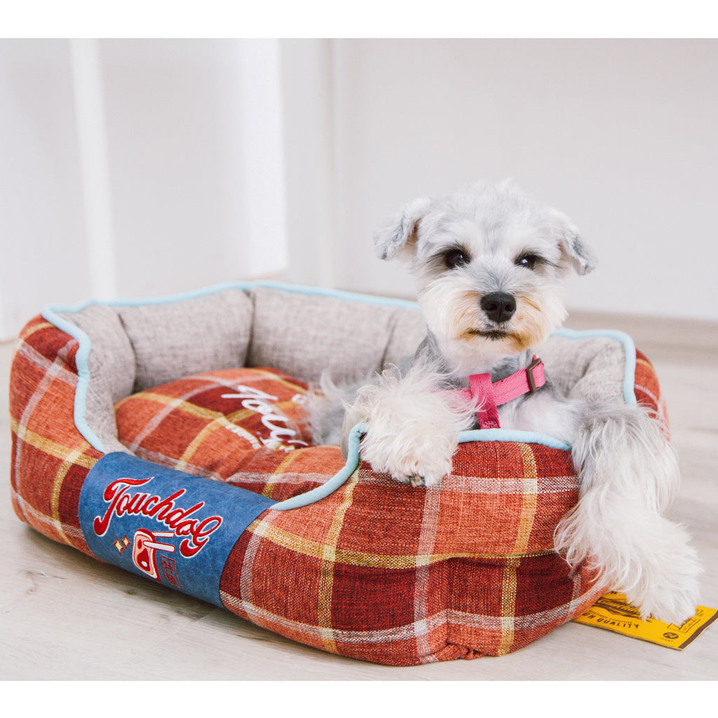 Red plaid oval dog bed with light blue trim; dog resting on cushion