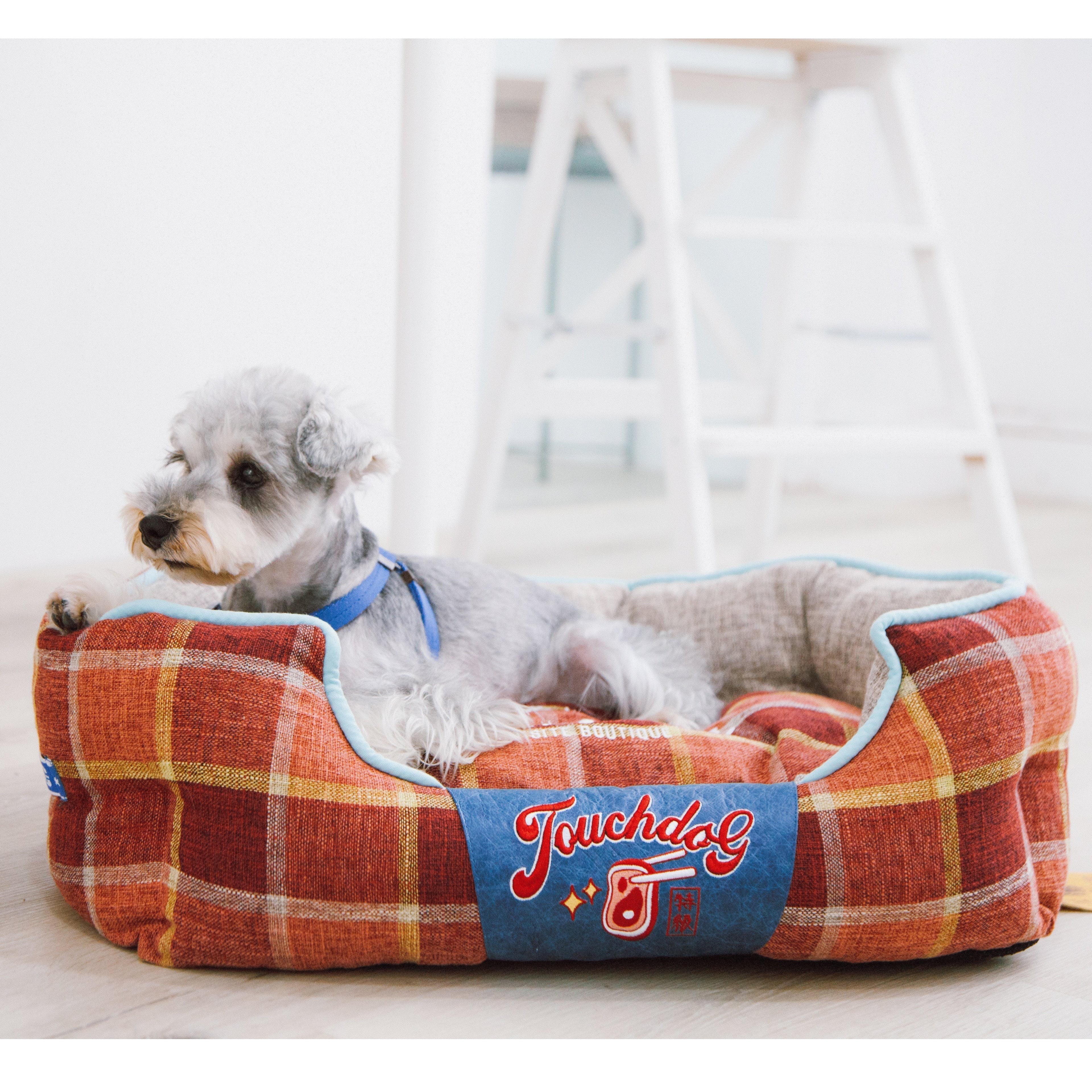 Red plaid oval dog bed with light blue trim and Touchdog logo, dog lying inside