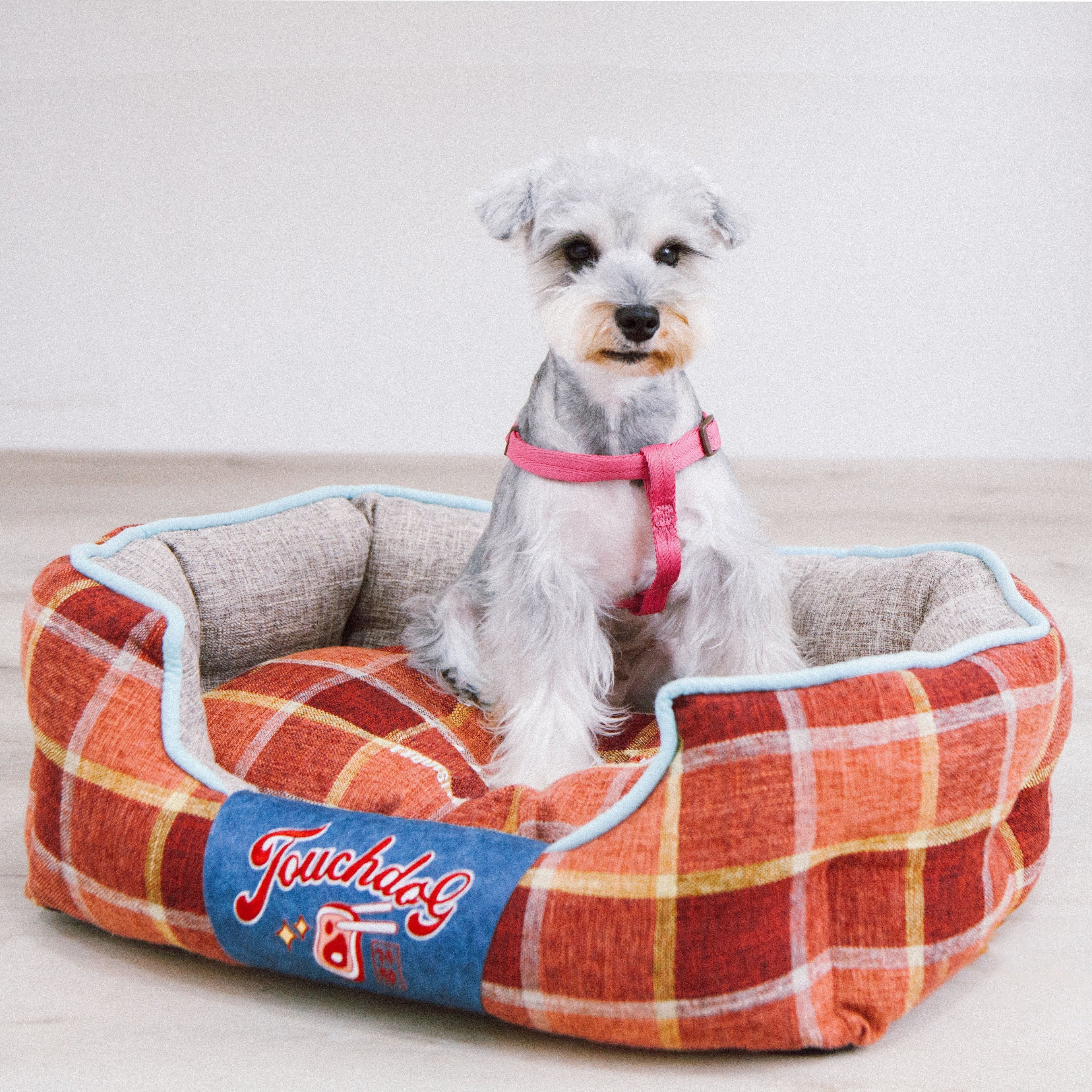 Red and yellow plaid oval dog bed with light blue trim, dog resting inside