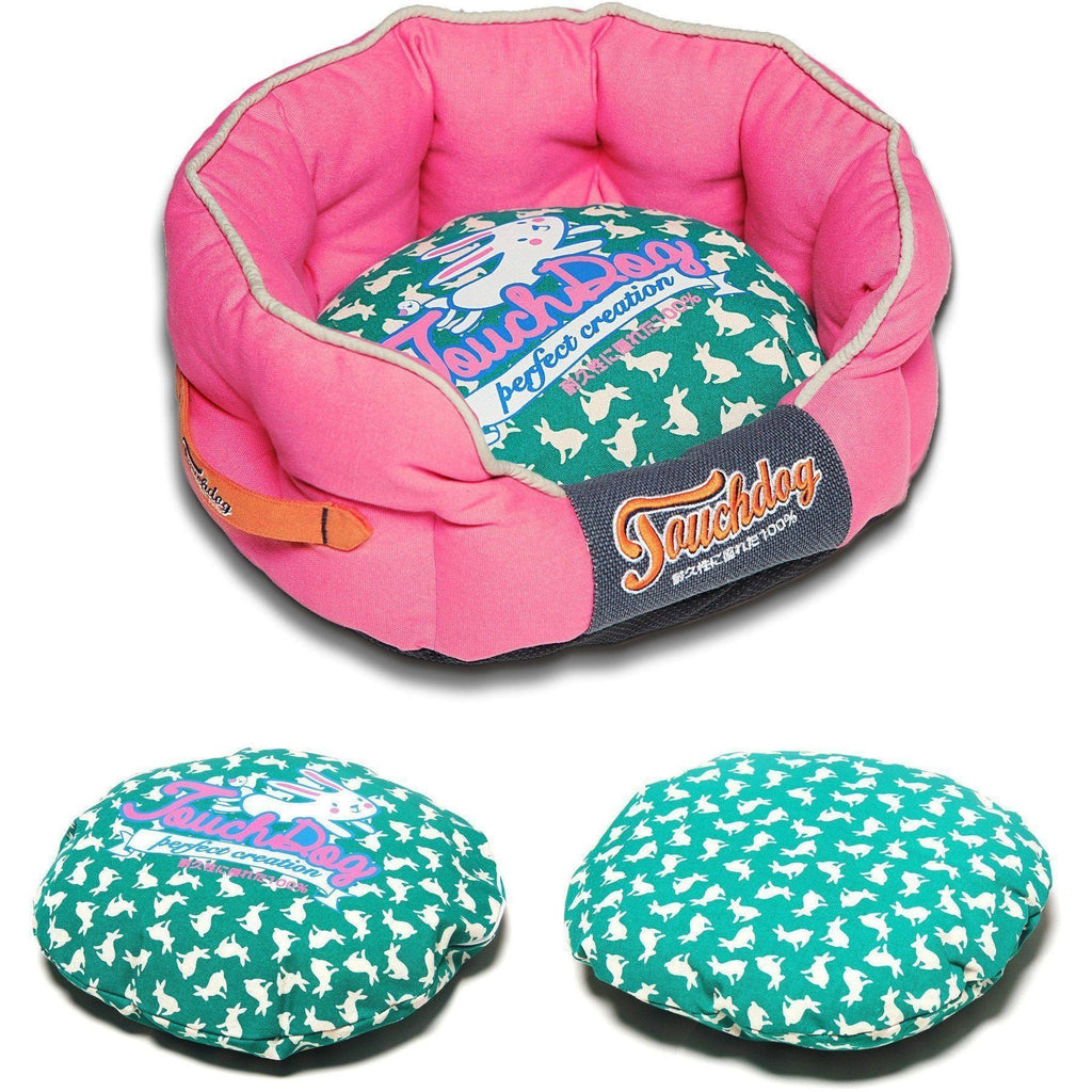 Pink rounded dog bed with teal rabbit-spotted cushion and navy logo panel