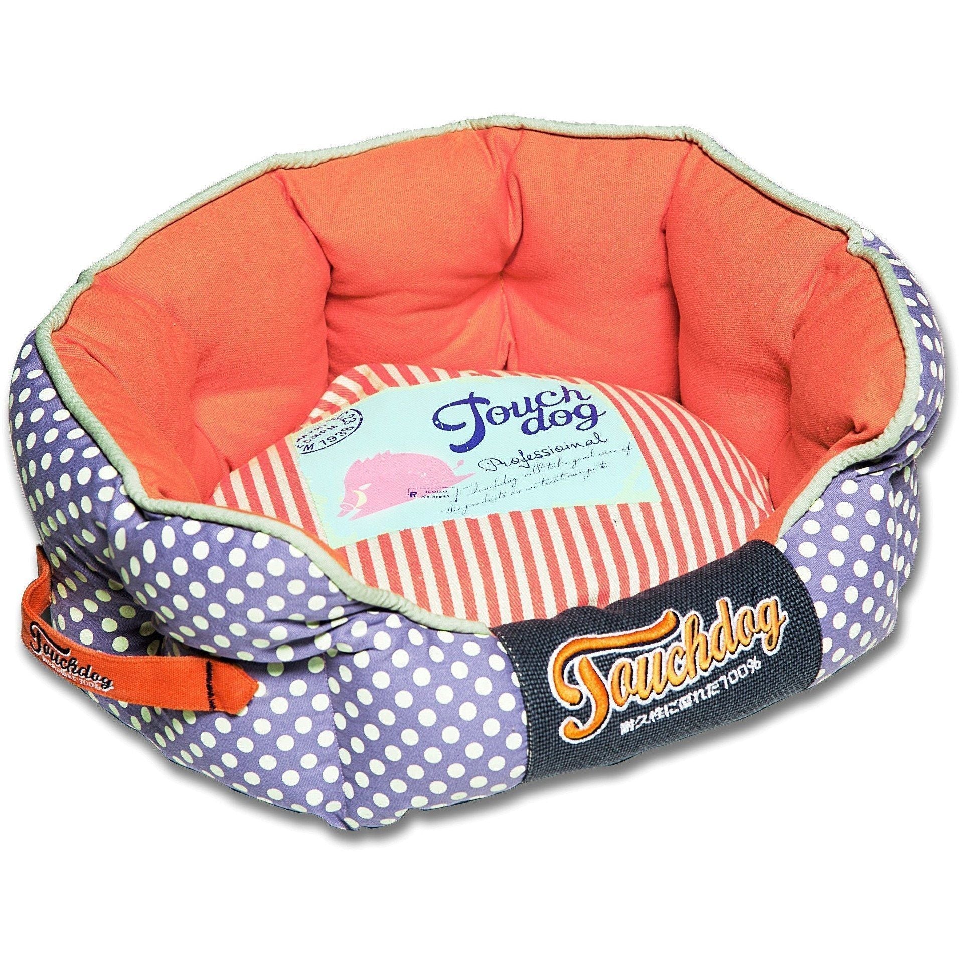Rounded dog bed with purple polka-dot sides, coral interior, striped insert, navy logo panel