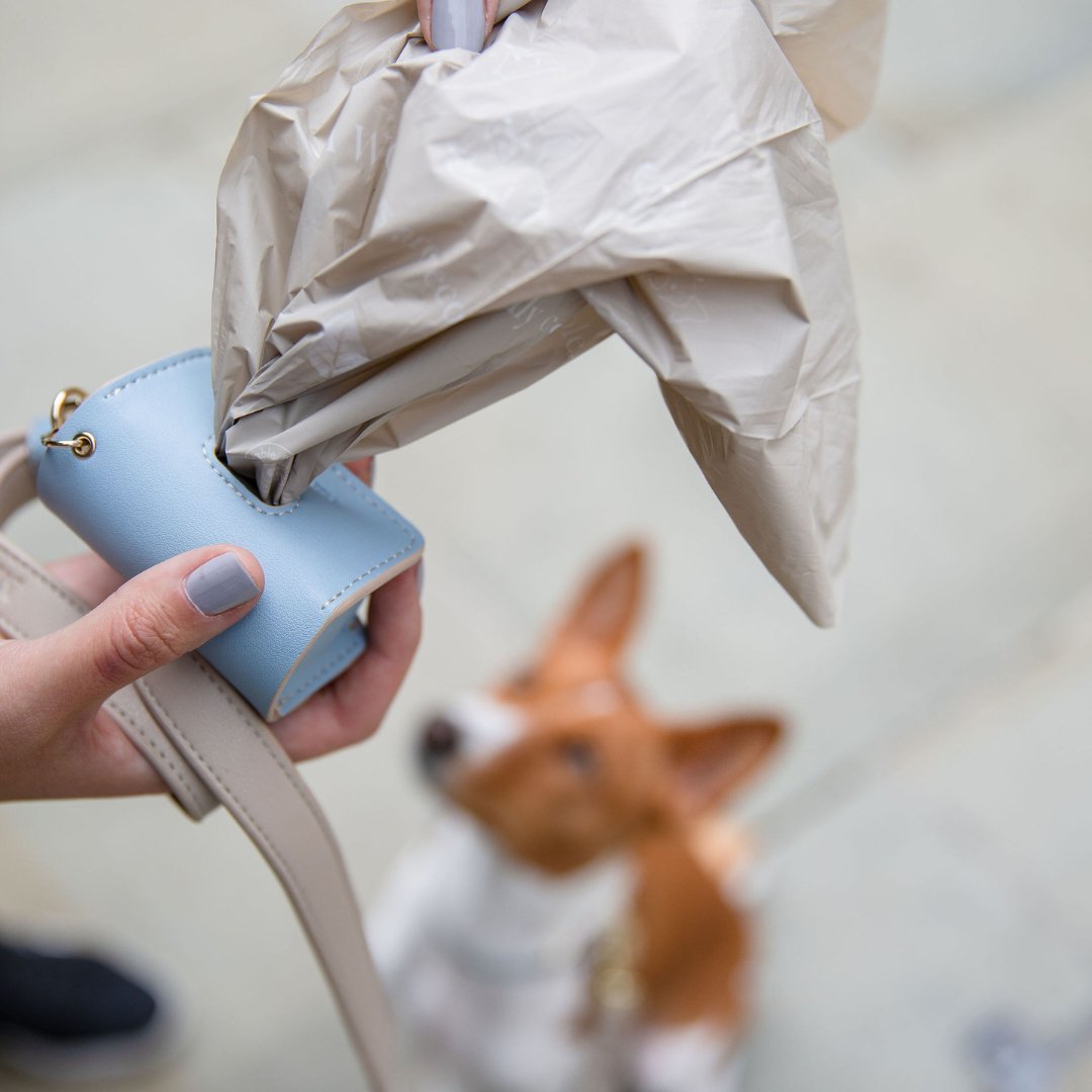 Blue waste bag holder clipped to a bag strap while dispensing dog waste bags