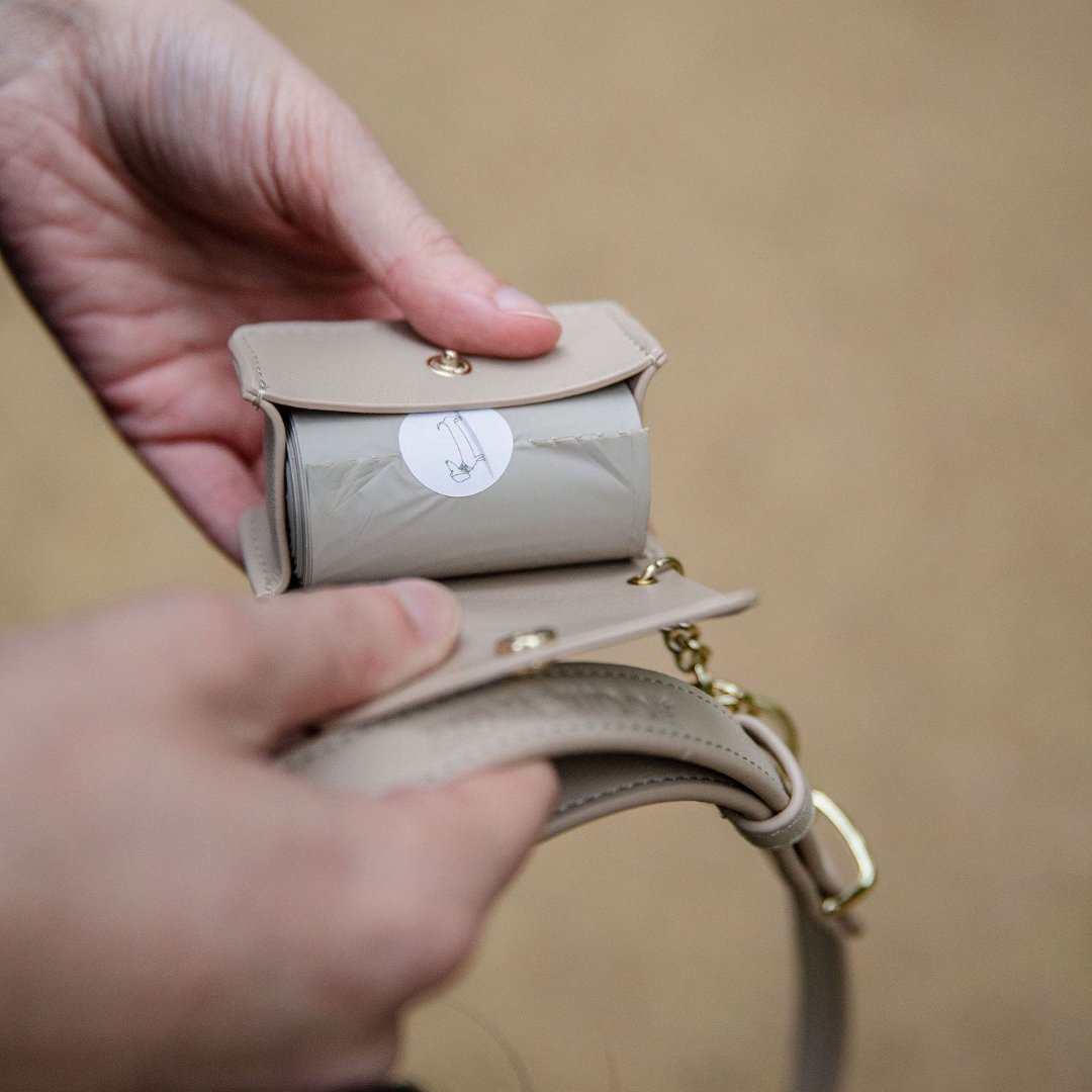 Beige waste bag holder with snap lid and keyring clip shown in a hand