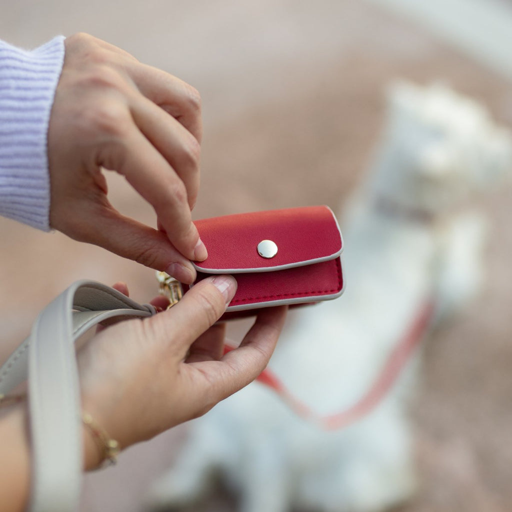 Red waste bag holder in hands, button snap closure and metal clip for leash